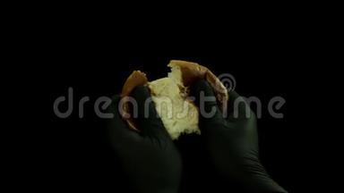 关闭面包师男子手撕裂热面包隔离在黑色背景。 库存录像。 用黑手套煮公手